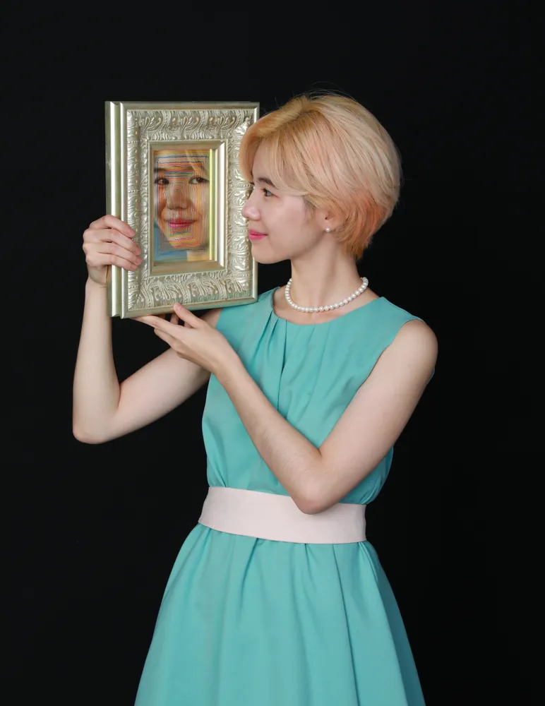 Joo Boram — portrait of the artist holding a small framed self-portrait drawing